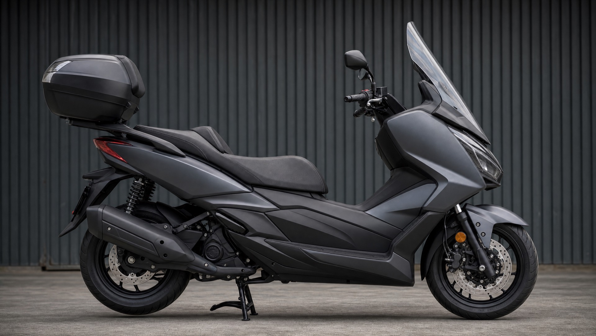 Maxi-scooter gris anthracite avec top-case et pare-brise, vu de profil dans un atelier.